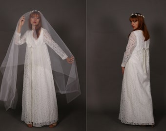 May include: A white lace wedding dress with long sleeves and a flowing skirt. The dress has a V-neckline and a delicate floral pattern. The model is wearing a white veil and a flower crown.