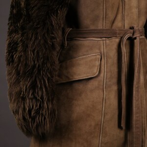 May include: A brown suede jacket with a fur collar and a tie belt. The jacket has a patch pocket on the front and is lined with a brown fabric.