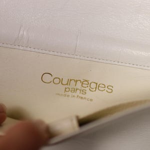 K&ouml;nnte beinhalten: Nahaufnahme des Inneren einer wei&szlig;en Lederhandtasche. Der goldene Text "Courr&egrave;ges paris made in france" ist sichtbar. Das Innere der Tasche ist cremefarben.
