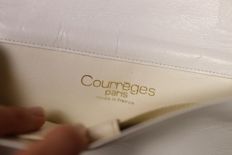 K&ouml;nnte beinhalten: Nahaufnahme des Inneren einer wei&szlig;en Lederhandtasche. Der goldene Text "Courr&egrave;ges paris made in france" ist sichtbar. Das Innere der Tasche ist cremefarben.