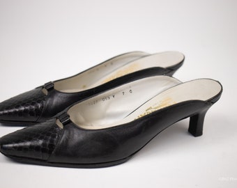 May include: Pair of black leather heeled mules with a snakeskin pattern. The shoes have a small bow detail on the front and a low heel.