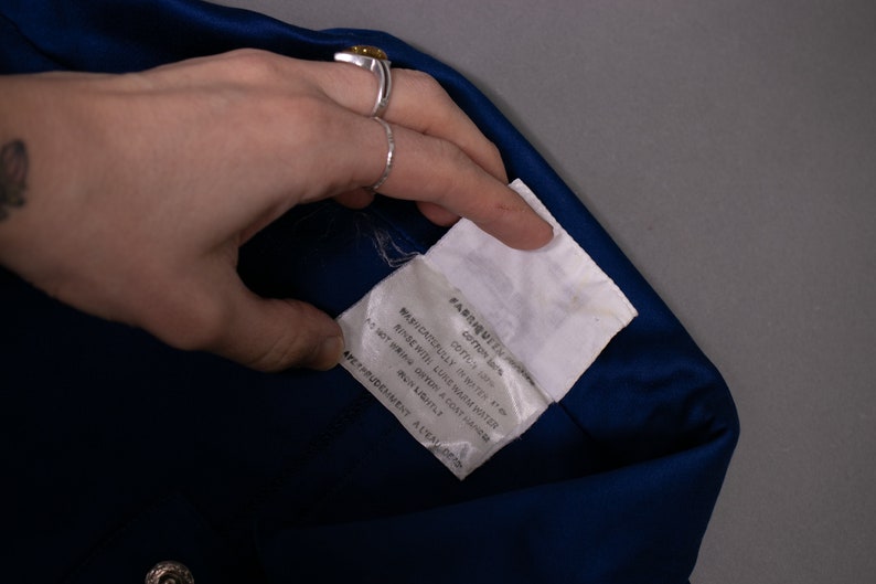 May include: A white fabric care label with black text that reads "FABRIQUEEN, COTTON 100%, CAFTLY SP, MAPUCATOFULLY IN WASH, AS NOT IRON ORTON A COAT HAMPER, RINSE WITH LUNE WARM WATER, DO NOT WRING, DRY LIGHTLY, APETPRUDENMENT A LEADERS".