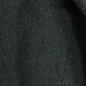 May include: Close-up of a dark green fabric with a subtle texture. The fabric has a small hole in the center.