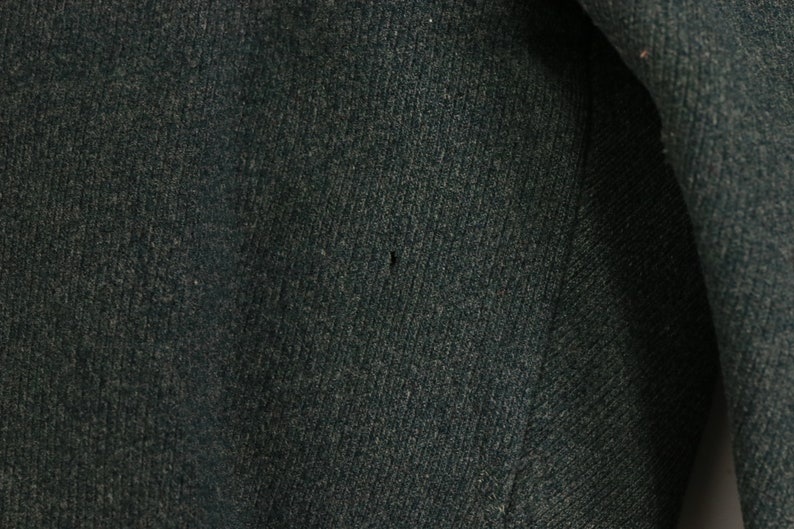 May include: Close-up of a dark green fabric with a subtle texture. The fabric has a small hole in the center.