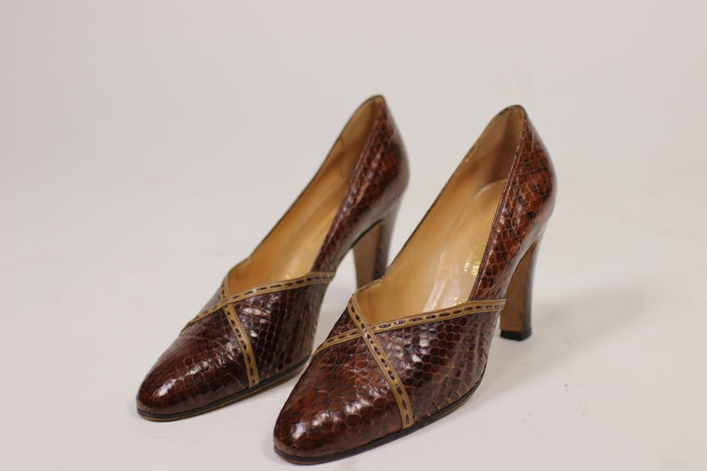 K&ouml;nnte beinhalten: Ein Paar braune, hochhackige Schuhe aus Leder mit Schlangenhautmuster und braunem Lederbesatz.