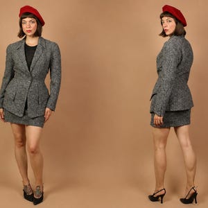 May include: A grey tweed blazer and matching mini skirt set paired with a red beret. The blazer features a single-button closure, notched lapels, and two front flap pockets. The skirt is a straight-cut mini length. The outfit is worn with black heels.