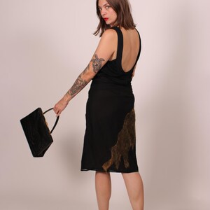 May include: A black dress with a low back and a knee-length skirt. The dress features a brown, textured design on the side. A black handbag with a handle is held in the hand. The person is wearing pink heeled sandals.