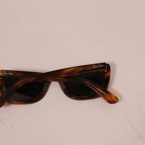 Puede incluir: Gafas de sol carey con lentes oscuras. Las gafas tienen una montura y patillas rectangulares cl&aacute;sicas. El logotipo de Ray-Ban es visible en las patillas. Las gafas est&aacute;n en &aacute;ngulo.