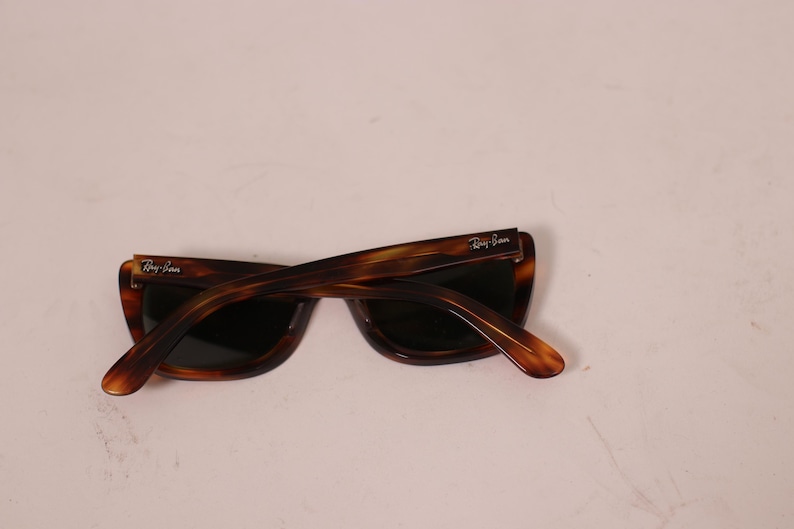 Puede incluir: Gafas de sol carey con lentes oscuras. Las gafas tienen una montura y patillas rectangulares cl&aacute;sicas. El logotipo de Ray-Ban es visible en las patillas. Las gafas est&aacute;n en &aacute;ngulo.