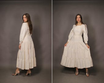 May include: A white tiered maxi dress with long sleeves and a square neckline. The dress is made of a lightweight fabric and has a flowy silhouette.