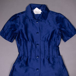 May include: A blue short-sleeved button-down shirt with a fitted waist and a collar. The shirt has a label that reads "Made in Italy".