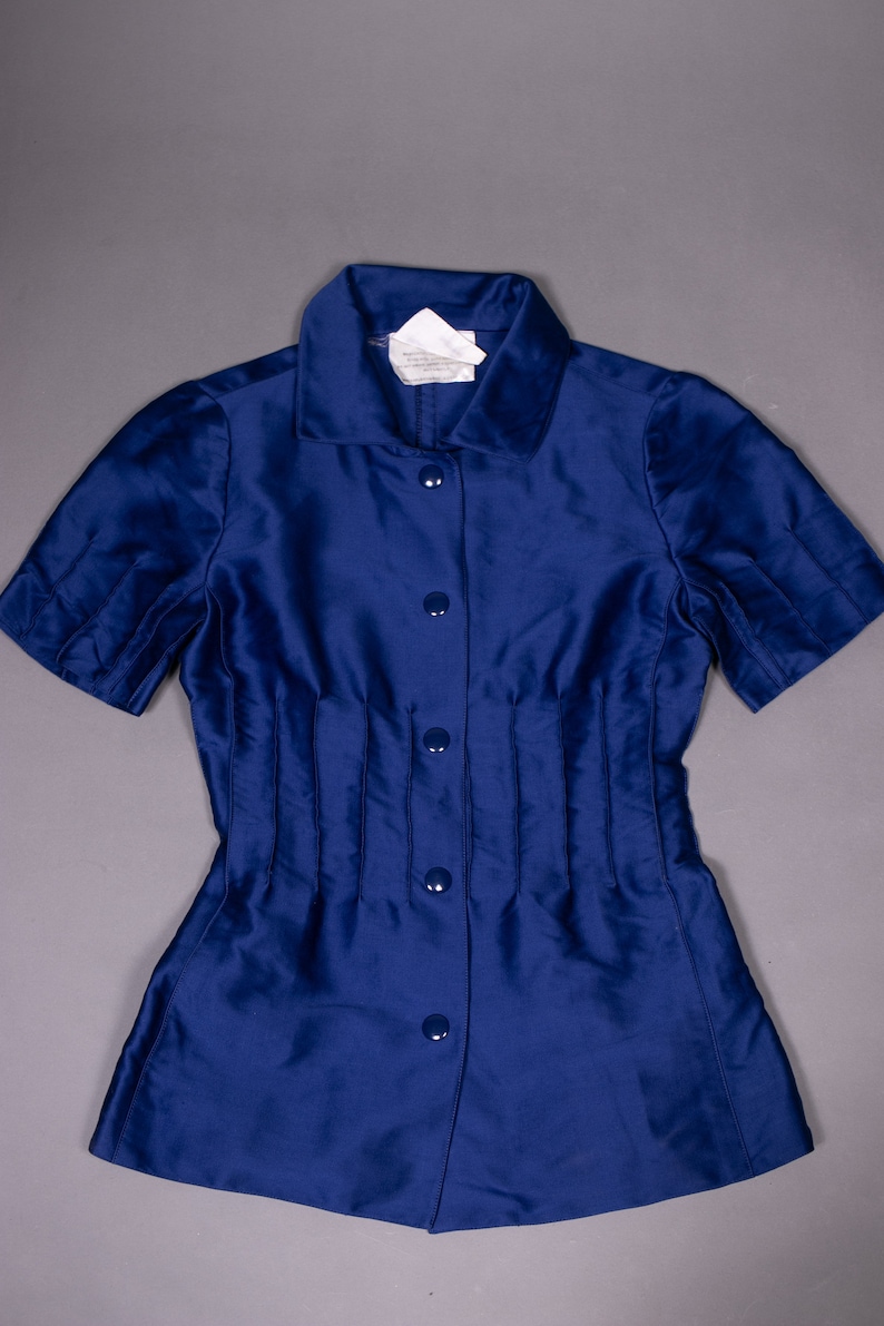 May include: A blue short-sleeved button-down shirt with a fitted waist and a collar. The shirt has a label that reads "Made in Italy".