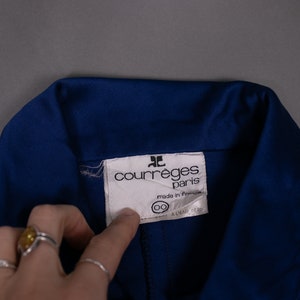 May include: A close-up of a blue collared shirt with a white label that reads "Courr&egrave;ges Paris" and "made in France".