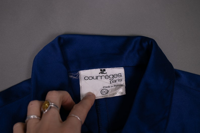 May include: A close-up of a blue collared shirt with a white label that reads "Courr&egrave;ges Paris" and "made in France".