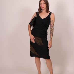 May include: A woman wearing a black dress with a V-neck and a knee-length skirt. The skirt has a brown, textured design. She carries a black handbag and wears light pink shoes.
