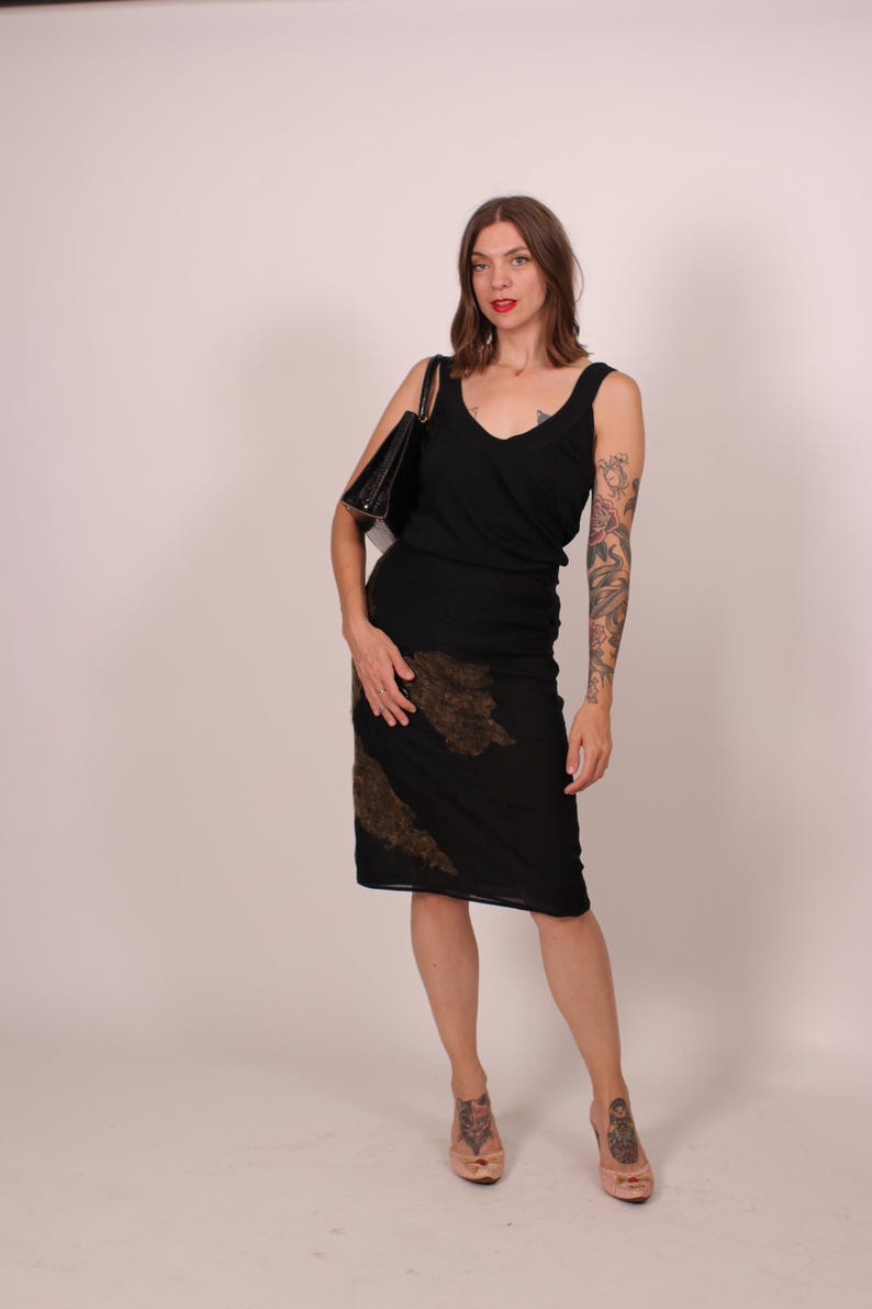 May include: A woman wearing a black dress with a V-neck and a knee-length skirt. The skirt has a brown, textured design. She carries a black handbag and wears light pink shoes.