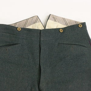 May include: A pair of dark green pants with a purple stripe down the side seam. The pants have a button fly and two back pockets.