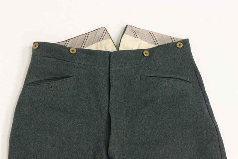 May include: A pair of dark green pants with a purple stripe down the side seam. The pants have a button fly and two back pockets.