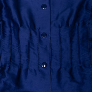 May include: A navy blue shirt with a button-up front and a series of vertical pleats. The shirt has three buttons.