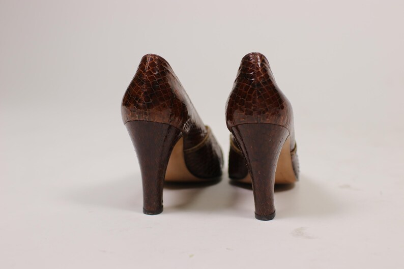 K&ouml;nnte beinhalten: Ein Paar braune Schlangenlederschuhe mit goldener Schnallenverzierung.