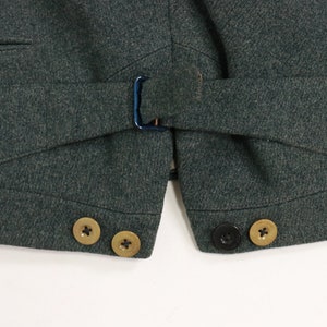 May include: A dark green vest with a belt and three gold buttons on the left side and two black buttons on the right side.