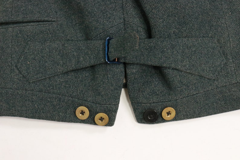 May include: A dark green vest with a belt and three gold buttons on the left side and two black buttons on the right side.