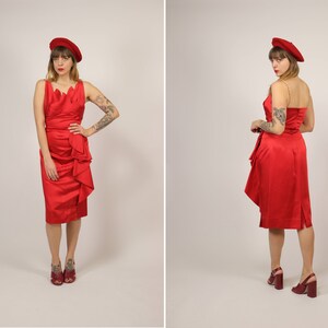 Könnte beinhalten: Ein rotes Satinkleid mit einem gerafften Rock und einem U-Boot-Ausschnitt. Das Kleid wird von einer Person mit Tätowierungen auf den Armen getragen. Die Person trägt eine rote Baskenmütze und rote Absätze.
