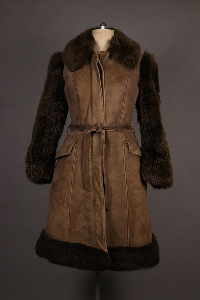 May include: A brown suede coat with a fur collar, cuffs, and hem. The coat has a belt and pockets.