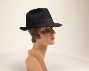 May include: A black fedora hat with a black band. The hat is on a mannequin head with brown hair.