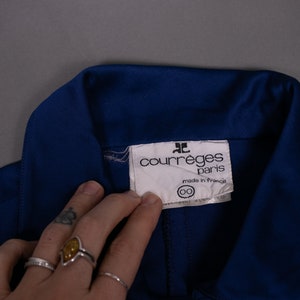 May include: A blue collared shirt with a white label that reads "Courr&egrave;ges Paris" and "Made in France".