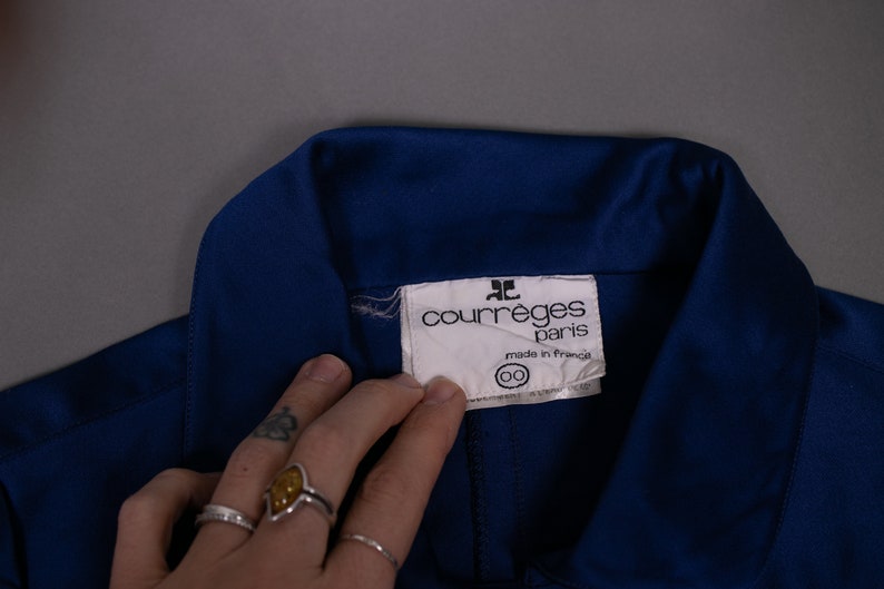May include: A blue collared shirt with a white label that reads "Courr&egrave;ges Paris" and "Made in France".