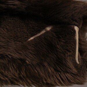May include: Close-up of a brown faux fur fabric with a white stitching detail.