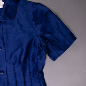 May include: A navy blue short-sleeved collared shirt with a button-up front and pleats on the front.