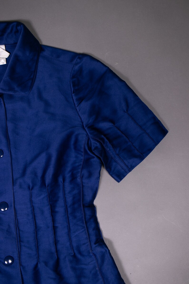 May include: A navy blue short-sleeved collared shirt with a button-up front and pleats on the front.