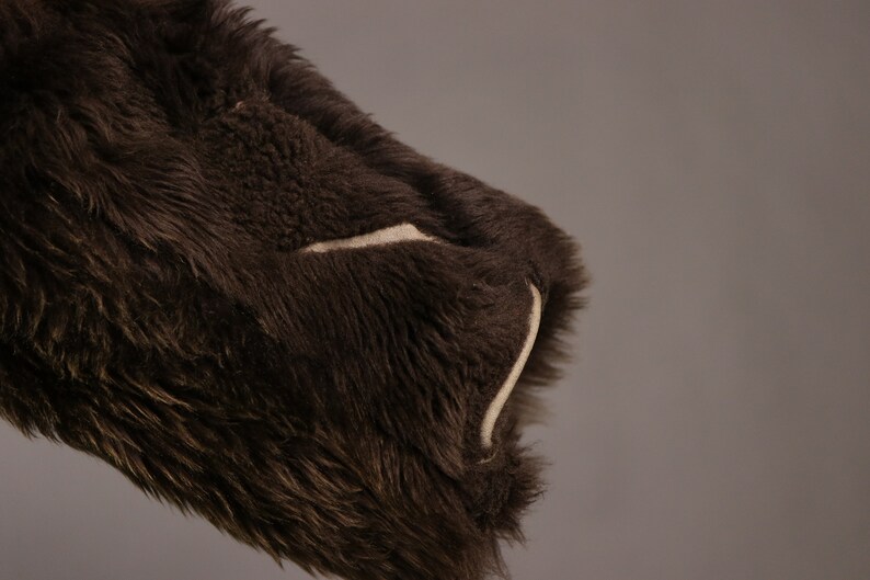 May include: Close-up of a brown faux fur jacket with a white seam detail on the sleeve.