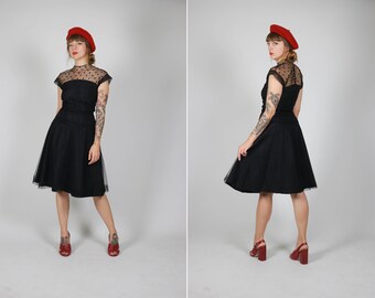 Può includere: Un abito nero vintage con gonna in tulle e maniche trasparenti a pois. L'abito è abbinato a un basco rosso e tacchi rossi. L'abito ha un corpetto aderente e una gonna svasata, creando una silhouette classica.