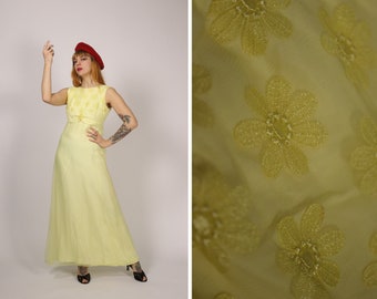 Puede incluir: Un vestido maxi amarillo pálido con un estampado floral. El vestido tiene un diseño sin mangas y un corpiño ajustado. El vestido está hecho de una tela transparente y tiene una falda fluida.