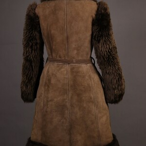 May include: A brown suede coat with a fur collar, cuffs, and hem. The coat has a belt and is lined with a brown fabric.