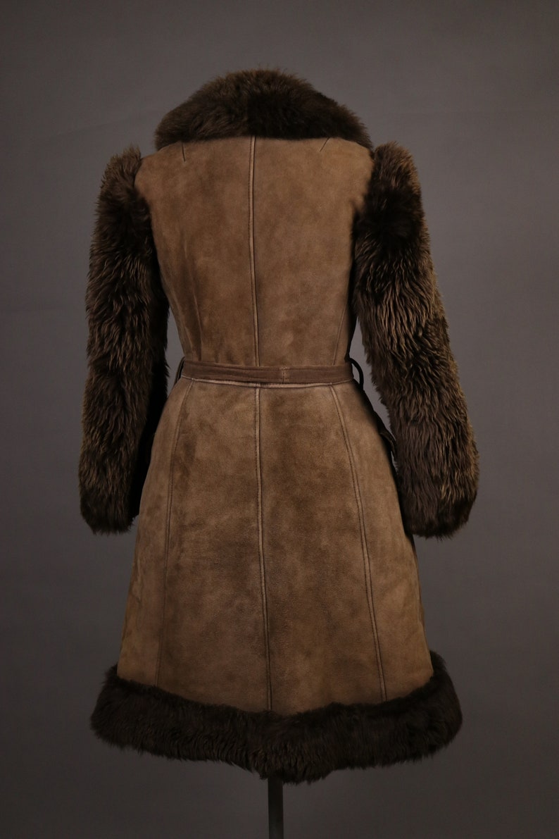 May include: A brown suede coat with a fur collar, cuffs, and hem. The coat has a belt and is lined with a brown fabric.