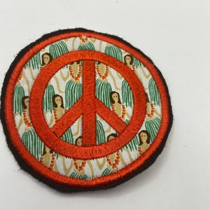 May include: A round, orange peace sign patch with a brown border. The patch is made of fabric and has a pattern of hula dancers in green grass skirts on a white background.