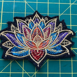 May include: A colorful embroidered patch featuring a stylized lotus flower with gold, blue, red, and purple accents. The patch is perfect for adding a touch of bohemian flair to clothing, bags, or other accessories.