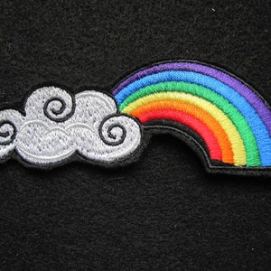 May include: A white embroidered cloud with a rainbow arch above it. The rainbow is made of red, orange, yellow, green, blue, and purple thread.