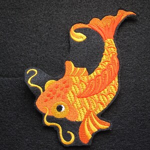 May include: An embroidered iron-on patch of a gold and orange koi fish with a curled tail. The fish is swimming upwards and has a black eye.