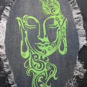 May include: Green embroidered design of a stylized face on a dark blue denim background. The design is surrounded by a frayed edge.