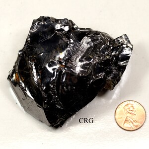 May include: A large, black, shiny, irregularly shaped piece of obsidian. The obsidian is about the size of a penny.
