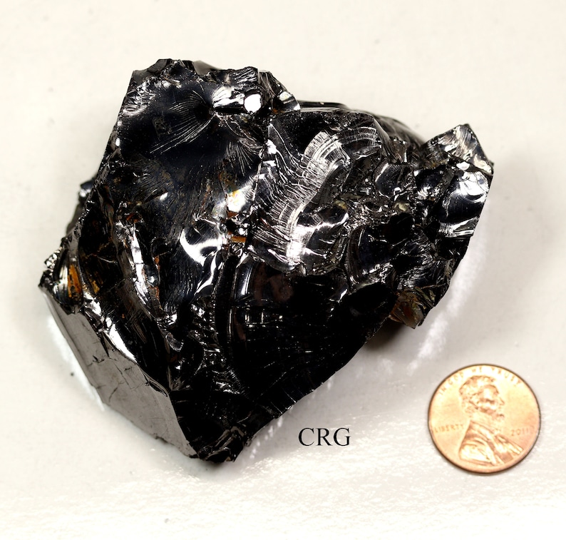 May include: A large, black, shiny, irregularly shaped piece of obsidian. The obsidian is about the size of a penny.