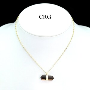 May include: A gold chain necklace with a brown crystal pendant. The pendant is a long, rectangular shape with a gold band around the center.