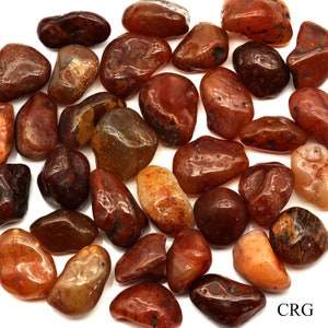 May include: A collection of carnelian tumbled stones in various shades of red, orange, and brown. The stones are smooth and polished, with a natural, earthy look.