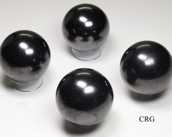 May include: Four polished, dark grey spheres, each resting on a small, clear stand. The spheres have a reflective surface, with subtle variations in tone. The spheres are arranged against a white background.