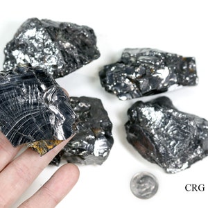 May include: Five pieces of raw, black, metallic, rough, and jagged,  cobalt ore. The ore is displayed on a white surface with a US dime for scale. The text "CRG" is printed in black on the white surface.
